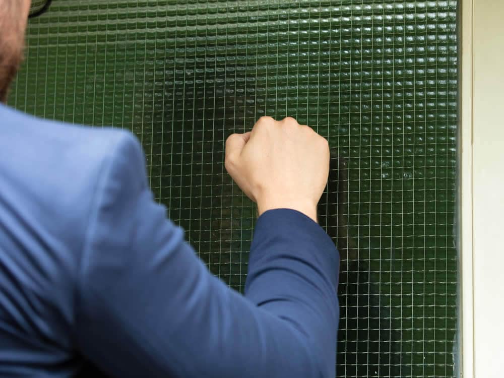 Gerichtsvollzieher in blauem Anzug klopft an eine Tür und versucht Mieter zu erreichen.