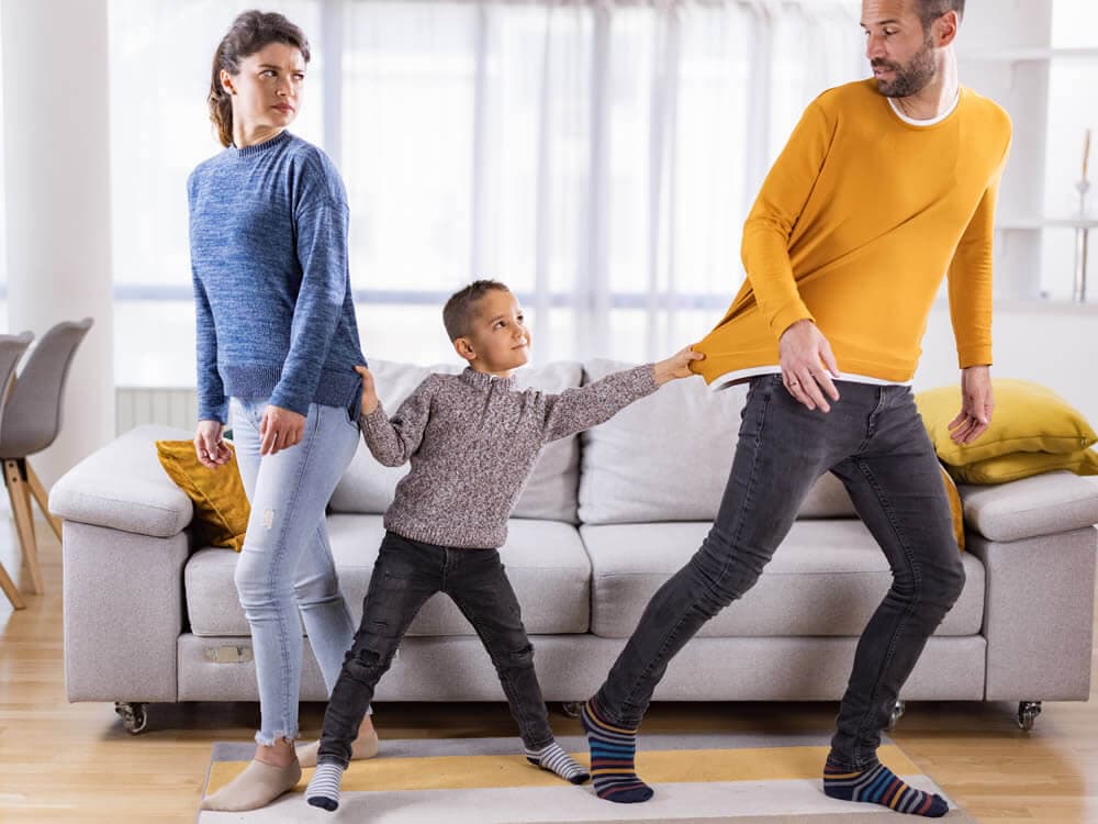 Ein Kind zieht spielerisch am Pullover eines Mannes, während seine Frau einen leicht abweisenden Gesichtsausdruck hat.