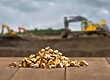 Ein Haufen Goldnuggets auf einer Holzoberfläche mit unscharfer Baumaschine auf Baugrundstück.