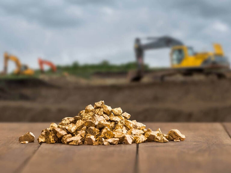 Ein Haufen Goldnuggets auf einer Holzoberfläche mit unscharfer Baumaschine auf Baugrundstück.