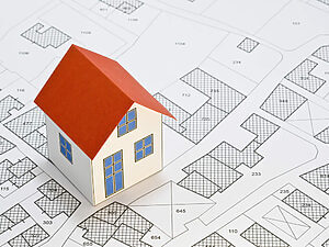 Ein kleines Haus mit rotem Dach auf einer Liegenschaftskarte, aus der Grundstücksaufteilungen und Grundstücksgrenzen sichtbar werden.