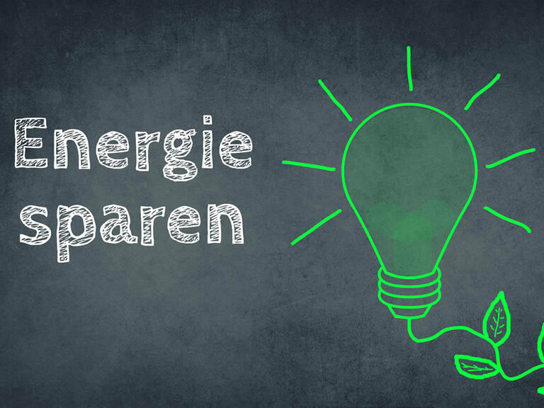 Tafel mit dem Satz „Energie sparen“ neben der Abbildung einer grünen Glühbirne mit Blättern, die Energieeinsparung im Immobilienbereich symbolisiert.