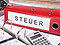 Roter Ordner mit der Aufschrift „Steuer“ auf einem Schreibtisch, umgeben von Papierkram und einem Taschenrechner, als Symbol für die Steuern, die in Zusammenhang mit einer Immobilie anfallen können.