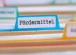 Eine Nahaufnahme von Karteikarten, mit einer blauen Karteikarte mit der Aufschrift "Fördermittel" im Mittelpunkt - ein wichtiger Begriff im geförderten Wohnungsbau.