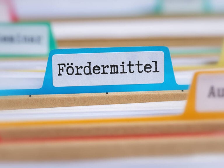 Eine Nahaufnahme von Karteikarten, mit einer blauen Karteikarte mit der Aufschrift "Fördermittel" im Mittelpunkt - ein wichtiger Begriff im geförderten Wohnungsbau.