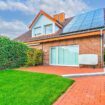 Eine verklinkerte Doppelhaushälfte mit rotem Dach und PV-Anlage, großen Fenstern und einem gepflegten, von Hecken gesäumten Rasen – idealer Hausverkauf in Gütersloh dank Immobilienmakler Immo Depot OWL.