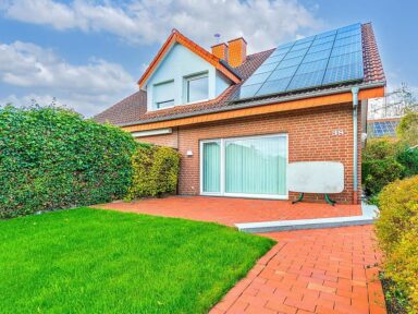Eine verklinkerte Doppelhaushälfte mit rotem Dach und PV-Anlage, großen Fenstern und einem gepflegten, von Hecken gesäumten Rasen – idealer Hausverkauf in Gütersloh dank Immobilienmakler Immo Depot OWL.