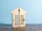 Ein ausgeschnittenes Holzhaus mit gepunkteten Linien und Scheren-Symbolen, die im Zusammenhang mit einer Teilungserklärung für eine Immobilie die Aufteilung symbolisieren, steht auf einer Holzfläche vor einem hellblauen Hintergrund.